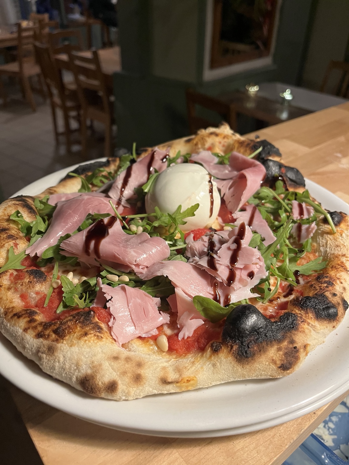 Pizza garnie de jambon, de roquette et d’une boule de fromage frais à L’Achillée