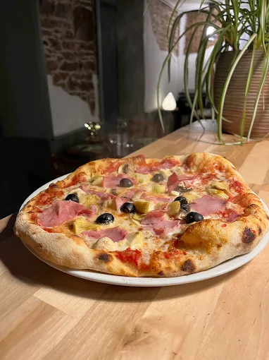 Pizza garnie de jambon, champignons et olives, à L’Achillée